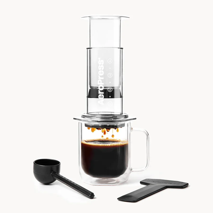 Transparent AeroPress Clear over a glass mug, with scoop and stirrer alongside