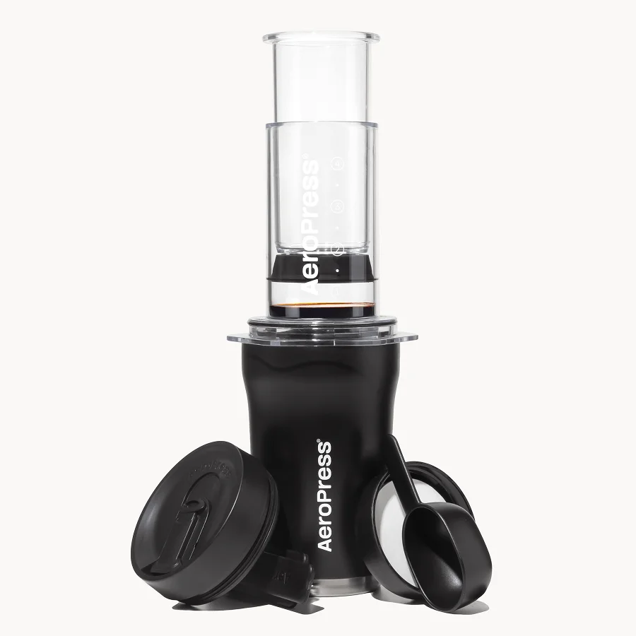 AeroPress Go Plus brewer on its black travel tumbler, with lid, scoop and stirrer