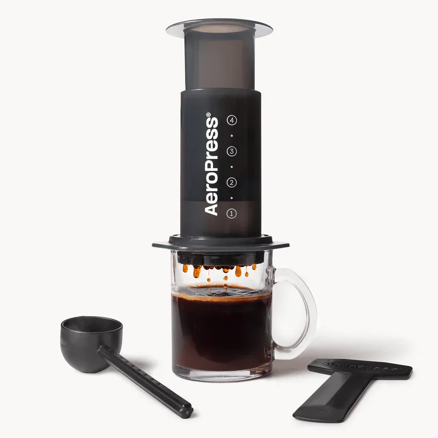 Smoky AeroPress Original over a glass mug, with scoop and stirrer alongside